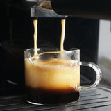 Espresso machine dispensing into a clear glass pitcher, layered coffee and crema