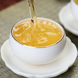 Yunnan Pu'er tea poured into a white ceramic teacup with gold rim on a woven surface