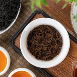 Wuyi Lapsang Souchong tea leaves steeped in a white bowl with two cups of amber tea on a tray