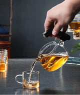 RORA glass teapot pouring amber tea into a glass cup with other cups nearby